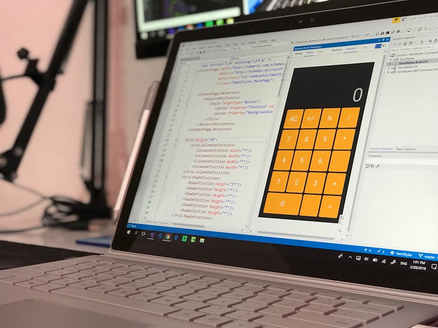 A close-up of a laptop on a desk displaying a programming environment with code on the left side of the screen and a large, orange calculator interface with basic functions on the right side. The back