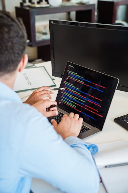 A close-up of a laptop on a desk displaying a programming environment with code on the left side of the screen and a large, orange calculator interface with basic functions on the right side. The back